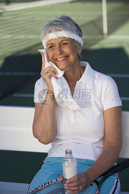 快乐的高级女性网球选手 水瓶用餐巾纸擦汗图片
