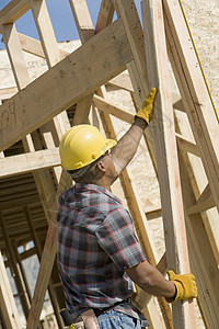 一名男子在建筑工地持有木梁的侧面视图图片