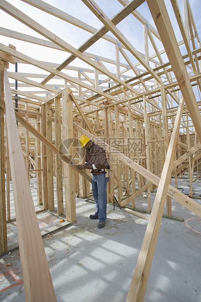 一名在建筑工地框架范围内测量木束的男子的全长视光图片