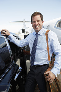 一个快乐的商务人士的肖像 带着行李坐在机场的汽车旁边图片