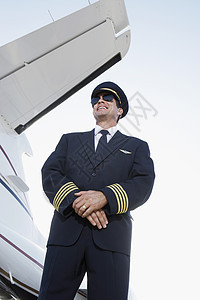 一个穿着制服的笑笑驾驶员 站在手拍着飞机旁边的低角度视角图片