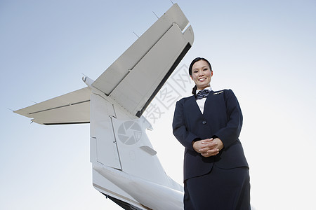 一个穿着制服的笑着空姐低角度肖像 站在私人飞机机翼下对天图片