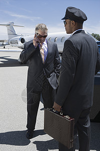 严重商务人士使用手机和汽车司机在机场拿着公事包的手提电话图片