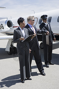 与同事同行的商务人士从机场司机手中拿公事包衣冠享受飞机合作商务旅行飞行员男子民航中年图片