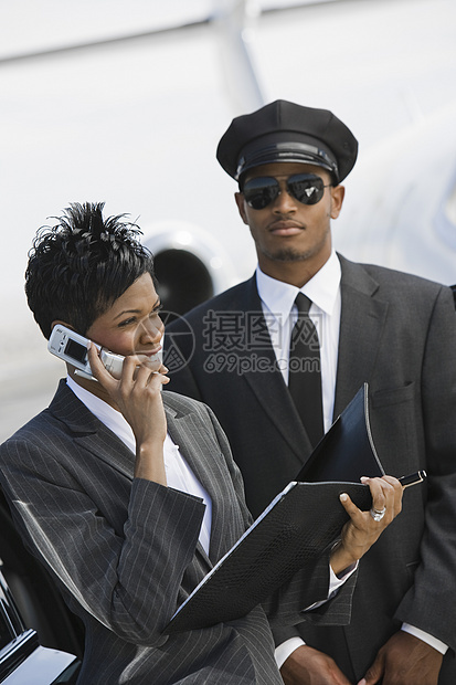 一名非洲裔美国女商务人士在机场后台使用手机 而司机站在后台图片