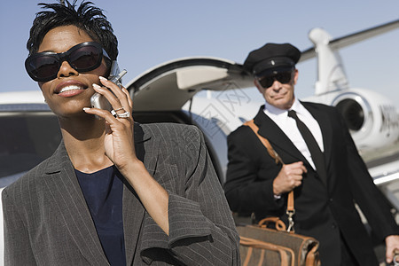 一名非裔美国商业女商务人士在机场与司机用手机进行交流 其背景是驾驶员图片