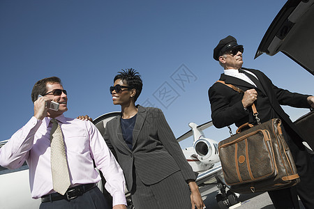 低角度视角 多族裔幸福的生意伴侣与司机在机场托着行李的驾驶员站在一起图片