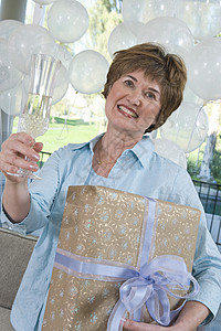 一个快乐的年长女子的肖像 拿着礼物和香槟笛子 在母鸡派对上图片