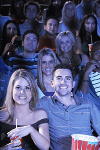 坐在剧院看电影的一对年轻夫妇肩膀旁成人两个人金发女郎爆米花朋友们大群人男子男人女士闲暇图片