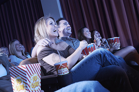欢笑的情侣在戏院看电影旁坐着双臂图片