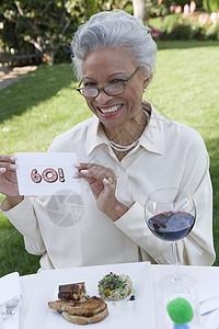 坐在桌上的酒杯和小点心上坐着的快乐老年妇女的肖像图片