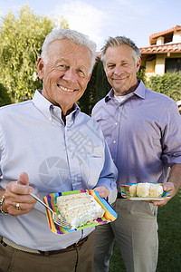 高级男性朋友在草坪吃蛋糕的肖像图片