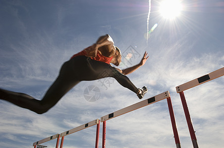 男性运动员在天空上跳跃障碍物的低角度视角男子奉献运动服双腿赛跑者轨道跨栏田径太阳专注图片
