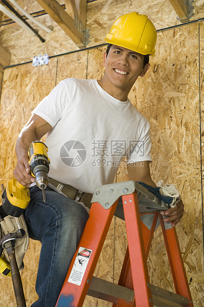 一名微笑着的中年建筑工人在扶持电力工具的梯子上的肖像图片