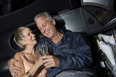 快乐的一对成熟的情侣举杯烤香槟 坐在豪华轿车和敬酒图片