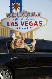幸福的成熟夫妇在豪华轿车中挥手 背景是“拉斯维加斯”标志图片