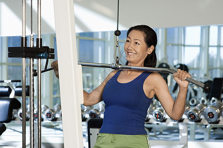 健身房的中国快乐女人 在拉拉机上举重图片
