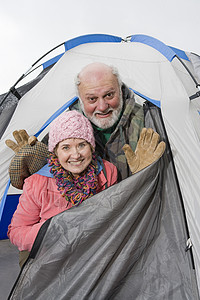 在露营帐篷外偷看头部的 快乐的老年情侣肖像眼神秃顶微笑个人冒险入口围巾假期胡须男士图片