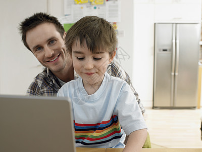 在家里使用笔记本电脑 将快乐的父亲和儿子与儿子的肖像描绘成图片