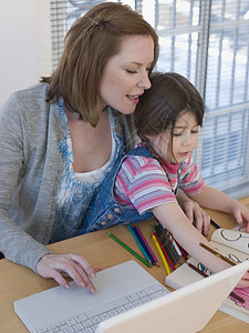母亲使用笔记本电脑 而女儿在家里桌子上染色书图片