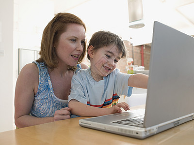 年轻女子和儿子在家里桌子上使用笔记本电脑图片