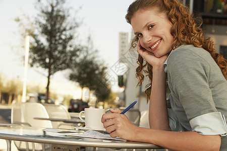 年轻女商务人士在户外咖啡馆拿笔的侧面肖像图片