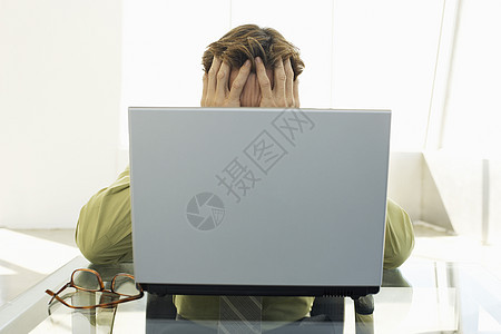 手持笔记本电脑坐在会议桌上的沮丧商务人士图片