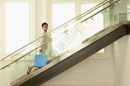 快乐的年轻女子带着购物袋走在现代楼梯上图片
