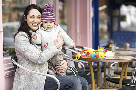 快乐的年轻母亲在咖啡厅坐在大腿上抱着婴儿的肖像椅子幸福帽子家长女孩团结孩子针织女性桌子图片