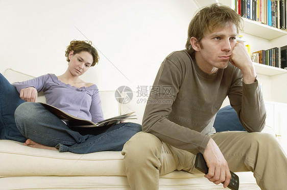 认真的青年男子在沙发上与妇女一起看电视图片