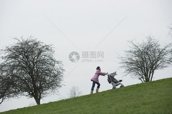 整个年幼母亲将婴儿车推上公园的山丘图片