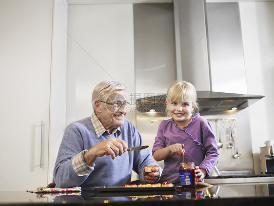 快乐的祖父和孙孙女在厨房吃烤面包和果酱图片