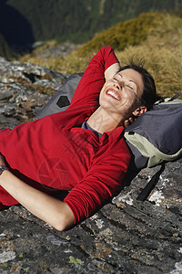 躺在巨石上头顶着背包微笑的年轻女子图片