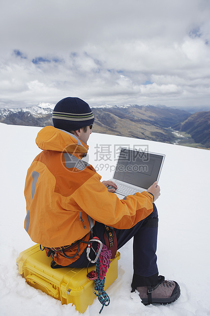 在雪山景观上使用笔记本电脑的男性远足者近视图片