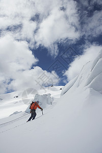 一只男性徒步者向雪山坡飞上云的侧面景色图片