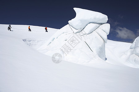 在雪山远处经过冰层形成 3个徒步登山者的侧面景色滑雪队形冒险家安全远足者成人领导探索者旅行绳索图片