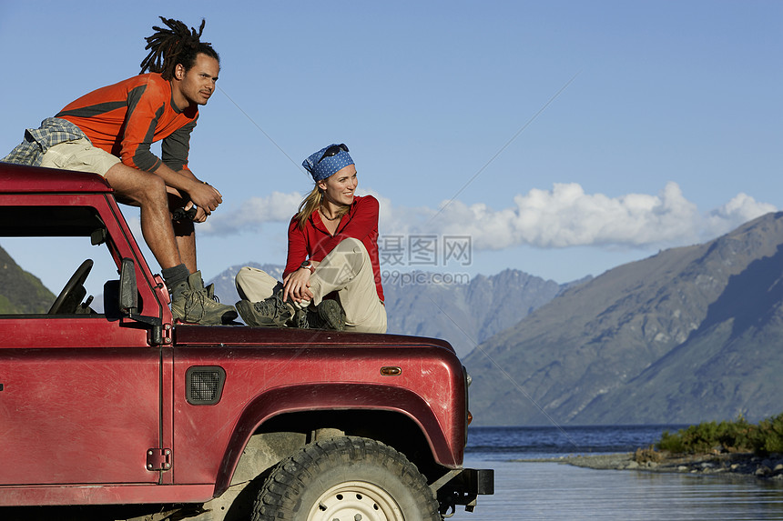 男人和女人坐在山湖附近的吉普车顶上图片