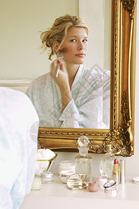 一位穿着浴袍的年轻女性坐在床上化妆时的反射产品腮红皮肤保养口红化妆品刷子金发女郎时间空闲图片
