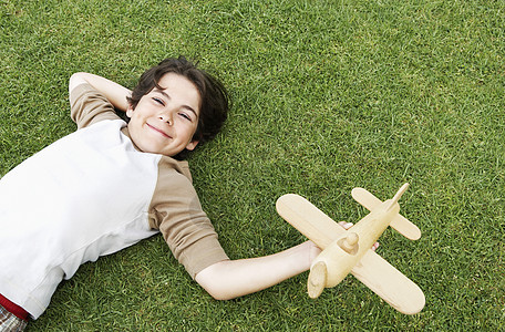 坐在草地上时拿着玩具飞机的可爱小男孩肖像图片