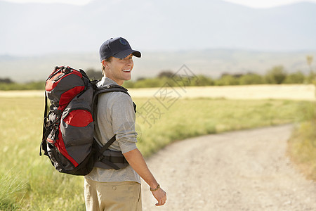 微笑的年轻男子与背背包在乡村公路上行走的肖像图片