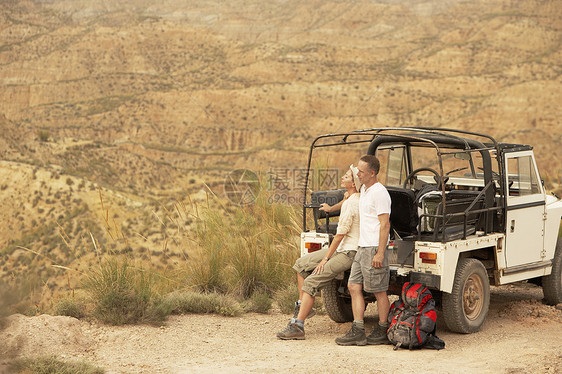 在沙漠悬崖边缘的四轮驱动汽车后面的中年夫妇图片