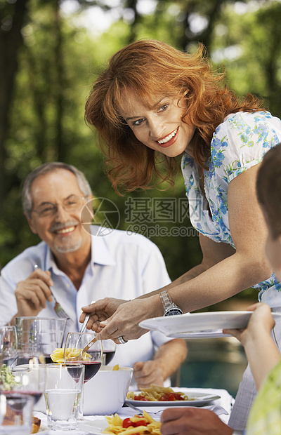 在后院的餐桌上为家庭提供食物的美丽妇女图片