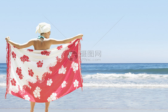 年轻女子在海滩上拿着沙龙的后视线图片