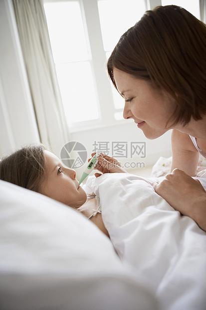 母亲检查在床上有温度计的女儿的体温女孩发烧女士卧室女性疾病孩子们团结羽绒被关爱图片