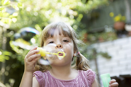 一个小女孩在后院吹肥皂泡的 紧闭专注孩子们气泡享受边缘乐趣娱乐长发快乐刘海图片