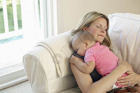 年轻金发母亲和婴儿在家沙发上睡着的年轻金发母亲图片