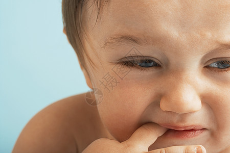 紧贴悲伤的婴儿男孩 用手指在嘴里 隔着蓝色背景与世隔绝图片