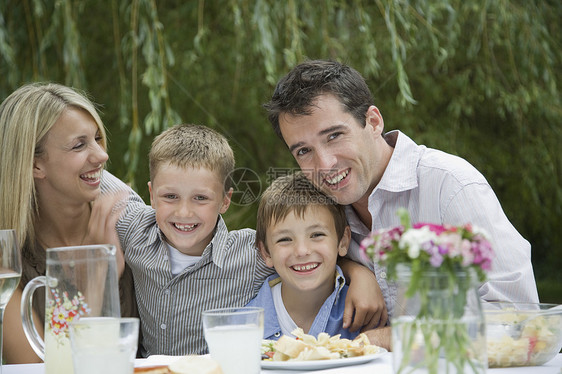 快乐父母的肖像与男孩一起在菜园餐桌上吃饭图片
