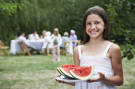 女孩(10-12)在花园家庭成员背景中持有的西瓜片(10-12)图片
