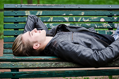 金发金发的年轻人 躺在公园长椅上图片